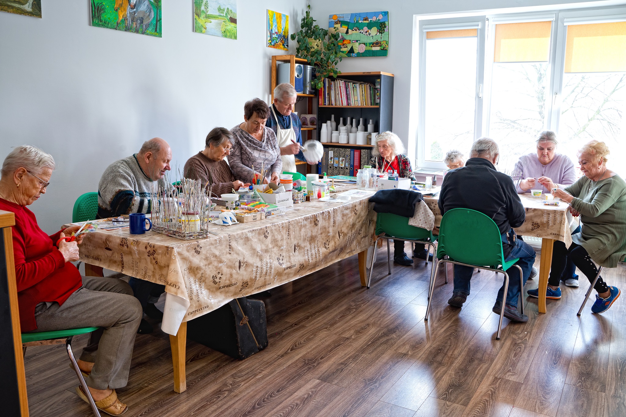 Na zdjęciu widać seniorów przy stole w kształcie litery L wykonujących ozdoby.
